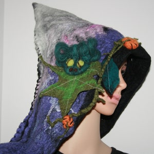 May include: A purple, black, and white hooded garment with a green leaf and orange pumpkin embellishments. The hood is decorated with a green felt creature with a white face.