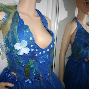 May include: A blue halter top with a sheer, ruffled overlay and blue and white flowers. The top is decorated with white beads and has a deep V-neckline.