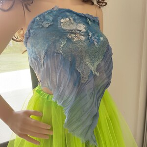 May include: A blue and white layered fabric top with a ruffled hem. The top is worn over a bright green tulle skirt.
