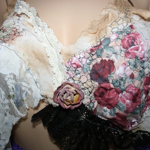 May include: A vintage-inspired top made from layers of lace, floral fabric, and sheer fabric. The top features a floral pattern with a brown, pink, and white colour scheme. The top is adorned with a large, brown flower.