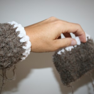 Puede incluir: Dos calientamanos marrones peludos con ribete de crochet blanco. Los calientamanos están hechos de un material suave y esponjoso.