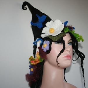 May include: A black felt hat with a whimsical design featuring flowers, mushrooms, and birds. The hat is worn on a mannequin with long black hair.
