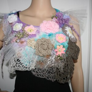 May include: A crocheted floral embellishment featuring a mix of pink, white, and brown flowers. The embellishment is crafted from a variety of textures and materials, including tulle, yarn, and fabric.