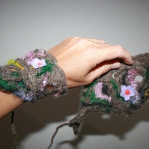 May include: Two brown wool wrist cuffs with colourful flower embellishments. The cuffs are made of felted wool and have a rustic, handmade look.