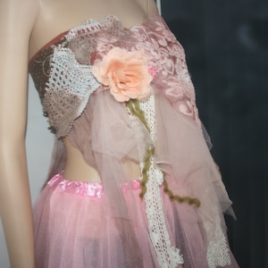 May include: A pink tulle skirt with a brown and white lace top. The top has a pink flower embellishment.