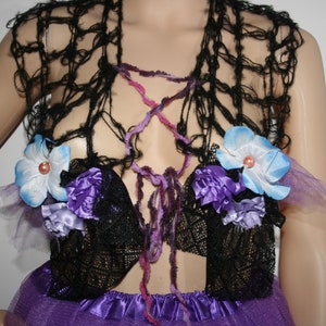 May include: A handmade, black crocheted top with a purple and pink laced bodice. The top features blue and purple floral accents with pearl centers. The bottom of the top is attached to a purple tulle skirt.