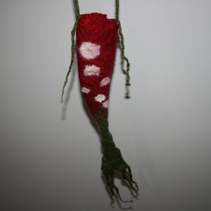 May include: A red felt pouch with white spots hanging from a green string. The pouch has a long, green felt tail.