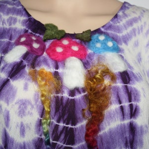 Puede incluir: Top morado sin mangas con estampado tie-dye con tres aplicaciones de champiñones de fieltro con tallos blancos y hojas verdes. Los champiñones son de color rosa, azul y morado con lunares blancos.