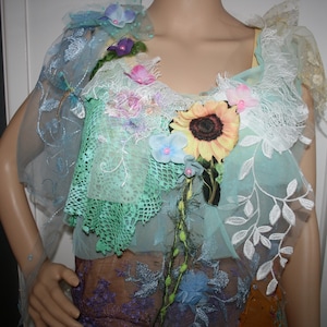 May include: A light blue sheer top with white lace and floral embellishments. The top features a sunflower, blue flowers, and green leaves.