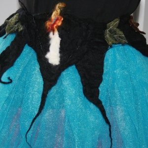 May include: A blue tulle skirt with a black felt applique. The applique is shaped like a butterfly with a white and orange centre.