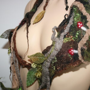 May include: A handcrafted felt bodice with a woodland theme. The garment features brown, green, and grey felt with leaf and mushroom accents. The design includes felted branches and leaves, creating a natural, organic appearance.