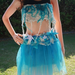 Puede incluir: Una falda azul y blanca de capas con adornos de flores blancas. La falda está hecha de una tela suave y fluida.