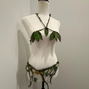 May include: A two-piece costume set featuring a halter top and a waist belt. The top is constructed from brown twig-like straps adorned with green fabric leaves. The belt consists of brown branches, green moss accents, and small hanging stones.