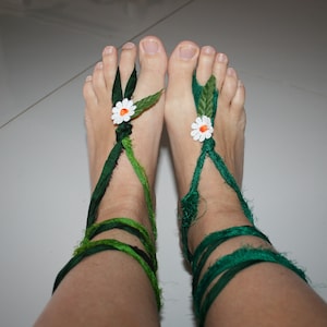 May include: A pair of green fabric sandals with white daisy flowers on each foot.