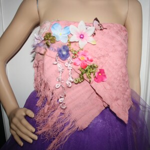 May include: A pink strapless dress with a floral embellishment on the bodice. The flowers are pink, white, blue, and green. The dress has a purple tulle skirt.