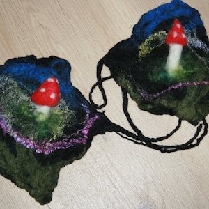 May include: Two felt mushroom ornaments with black, green, blue, and purple accents. Each ornament features a red and white mushroom with a white stem.