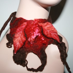 May include: A brown and red felted wool neck scarf with two large red leaves attached. The scarf is tied around a mannequin's neck.