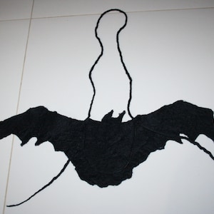 May include: Black felt bat wings with a black felt loop for hanging. The wings are spread out and the loop is at the top.
