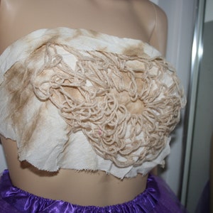 May include: A white fabric top with a brown crocheted design. The top is strapless and has a raw edge.