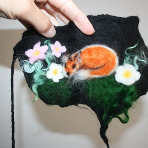 May include: A felt wall hanging with a sleeping fox, green foliage, and pink and white flowers.