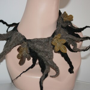 May include: A felted necklace with a nature-inspired design. The necklace features a gray and black color scheme, with leaf accents in shades of brown and green. The design resembles tree branches.