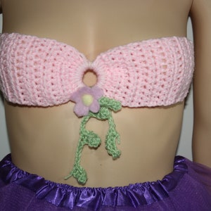 May include: A pink crocheted bandeau top with a flower and leaves embellishment. The top is worn on a mannequin with a purple tulle skirt.