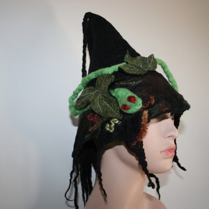 May include: A black felt witch hat with green and red felt leaves and vines. The hat has a long, flowing brim and is decorated with intricate details.
