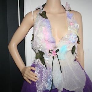 May include: A white halter top with a floral design. The top is made of a soft, flowing fabric and features a variety of flowers in shades of pink, purple, and blue. The top is tied at the neck and has a loose, flowing fit.