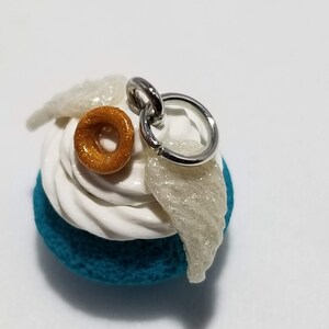 Peut inclure: Un charme bleu sarcelle, blanc et or avec un beignet, du gla&ccedil;age et des ailes. Le charme a un anneau de saut argent&eacute; pour l'attacher &agrave; un collier ou un bracelet.