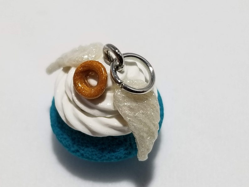 Peut inclure: Un charme bleu sarcelle, blanc et or avec un beignet, du gla&ccedil;age et des ailes. Le charme a un anneau de saut argent&eacute; pour l'attacher &agrave; un collier ou un bracelet.