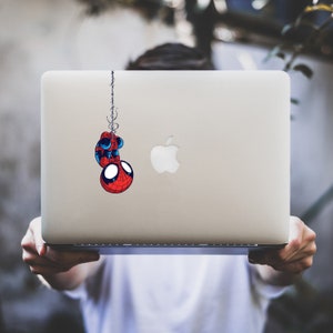 Op de afbeelding: Een zilveren laptop met een rode en blauwe Spiderman-sticker op de deksel. De sticker toont Spiderman die ondersteboven aan een spinnenweb hangt.