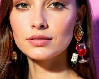 May include: Dangling earrings featuring miniature wine bottles and wine glasses. The earrings have red, green, and gold accents. The background is a solid pink color.