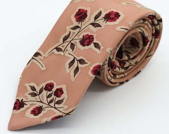 May include: A peach-colored tie with a floral pattern featuring red roses and brown stems. The tie is made of a textured fabric and is rolled up.