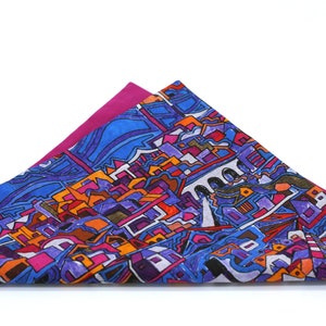 May include: A colorful silk scarf with a geometric pattern of buildings and water. The scarf is folded in a triangle shape and has a pink underside.