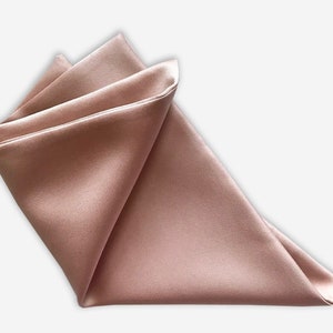 May include: A folded, satin pocket square in a muted rose color. The fabric has a subtle sheen, and the edges are neatly folded into a triangle shape. The pocket square is a formal accessory.