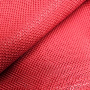 May include: Close-up of a textured red fabric with a repeating pattern of small, interconnected shapes. The fabric is folded, revealing layers and shadows that highlight the texture and depth of the material. The color is a vibrant, solid red.