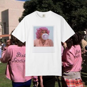 Può includere: Una t-shirt bianca a maniche corte con una stampa grafica rettangolare centrata raffigurante una persona con capelli rosa acceso che soffia una grande bolla di gomma da masticare rosa, indossando una camicia a colletto rosa chiaro e una collana di perle bianche.