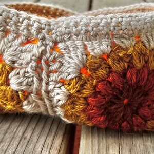 May include: A crocheted basket with a white, orange, and brown floral pattern.