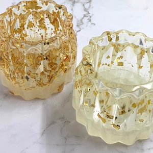 May include: Two clear glass candle holders with a textured, wavy design. The holders are filled with gold leaf flakes.