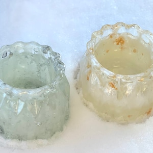 May include: Two clear glass candle holders with a textured, frosted finish. The candle holder on the left is a light green color, while the candle holder on the right is a light yellow color.