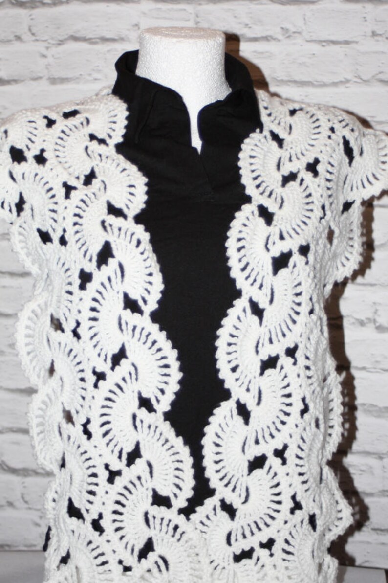 May include: White crocheted shawl with a delicate, lacy pattern. The shawl is draped over a black shirt.