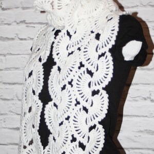 May include: White crocheted scarf with a delicate floral pattern. The scarf is draped over a black shirt.