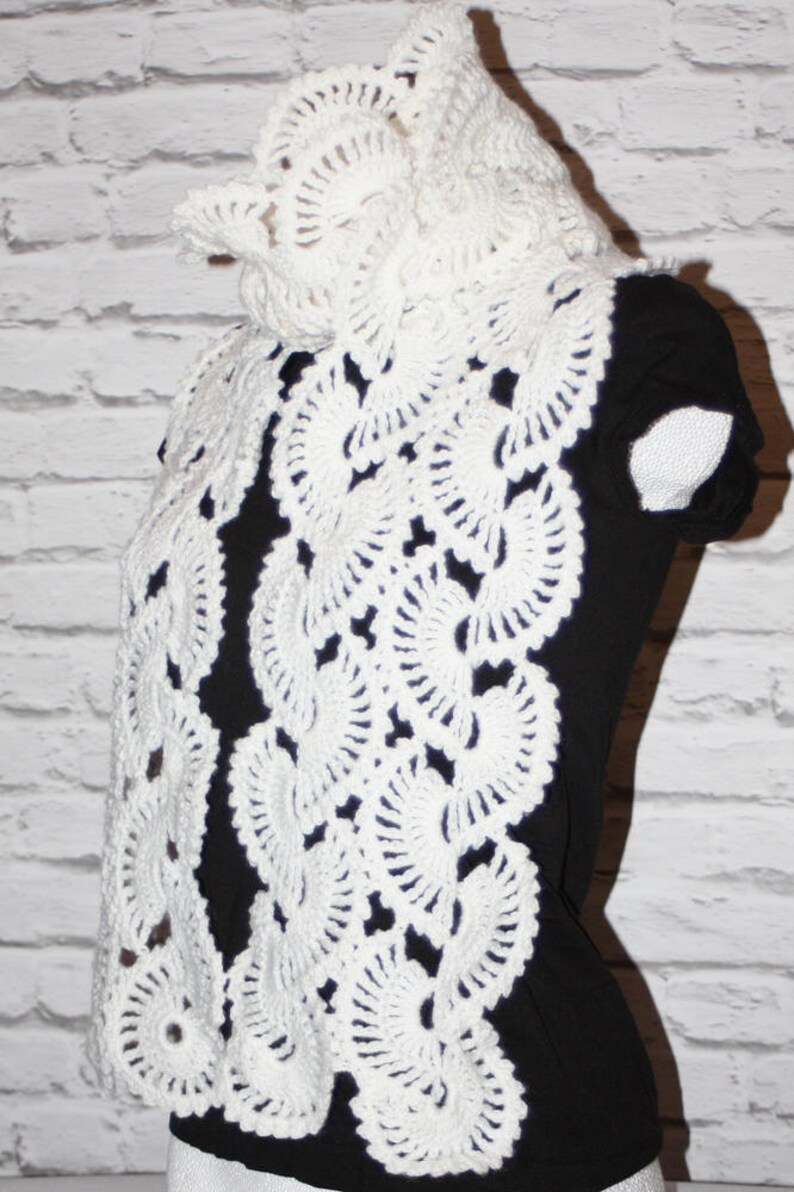 May include: White crocheted scarf with a delicate floral pattern. The scarf is draped over a black shirt.