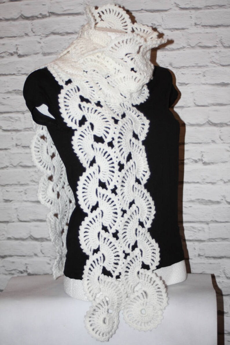 May include: White crocheted scarf with a lacy design featuring a series of circular patterns. The scarf is draped over a black mannequin.