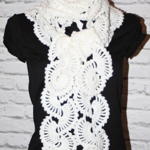 May include: White crocheted scarf with a delicate, lacy design. The scarf is draped over a black shirt.