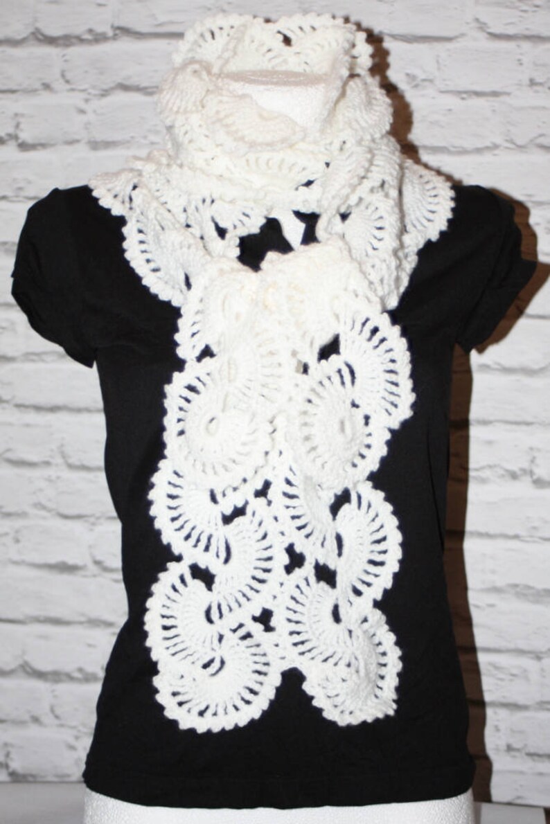May include: White crocheted scarf with a delicate, lacy design. The scarf is draped over a black shirt.