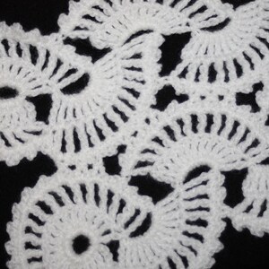 May include: White crocheted lace with a delicate floral pattern. The lace is made up of small, intricate circles and swirls.