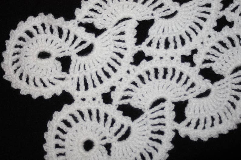 May include: White crocheted lace with a delicate floral pattern. The lace is made up of small, intricate circles and swirls.