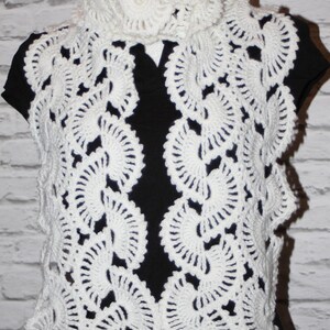 May include: White crocheted scarf with a delicate, lacy pattern. The scarf is made of a soft, lightweight yarn and features a circular design.