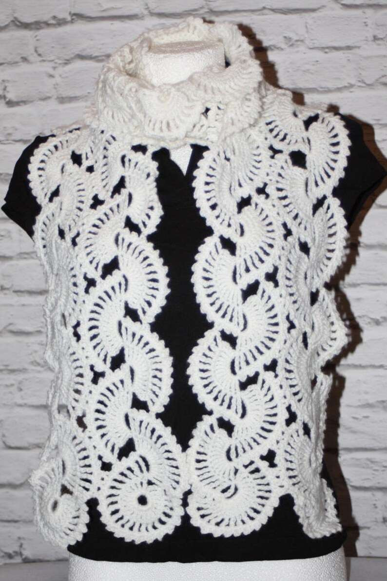 May include: White crocheted scarf with a delicate, lacy pattern. The scarf is made of a soft, lightweight yarn and features a circular design.